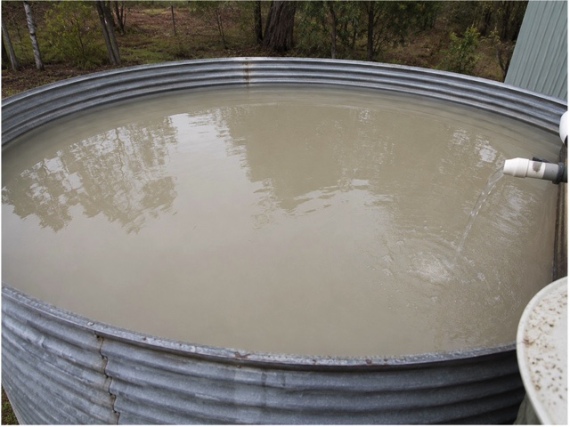 Looking down into a rainwater tank filled with milky, grey-brown water