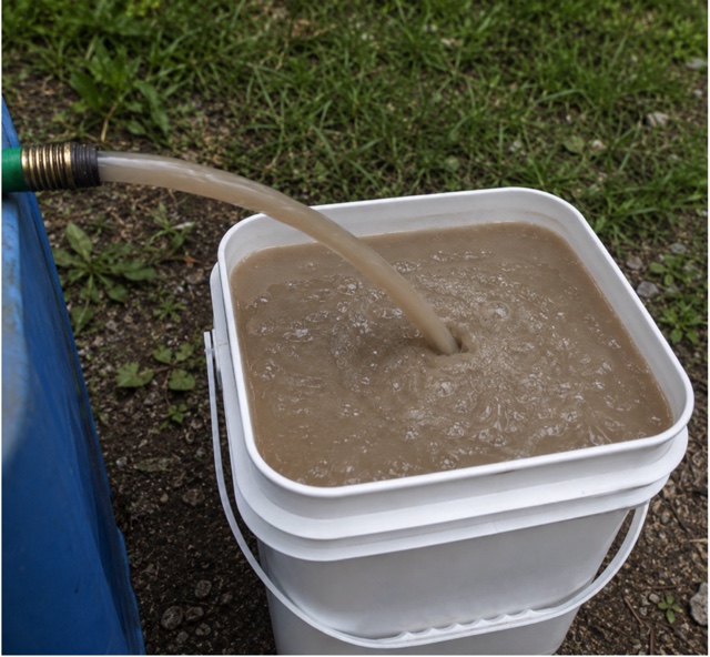 An open-top steel rainwater tank full of turbid brown water with the inlet still running