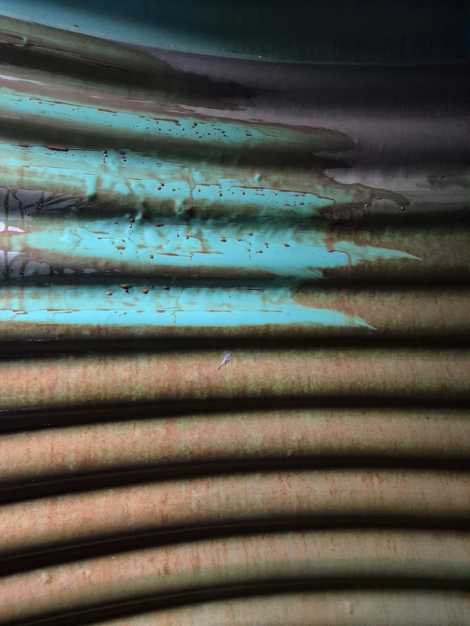 A brown sticky film on the corrugated wall of a rainwater tank, partly wiped away to show the clean surface beneath